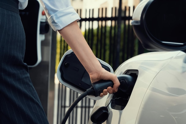 Focus EV charger plug with blur progressive woman charge EV car in background