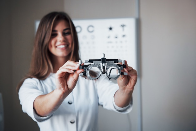 Focus on the glasses. Female doctor standing in the office and holding special eyeglasses with board for testing visual acuity