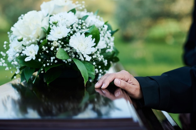 Focus on hand of mourning mature woman in black attire on lid of coffin