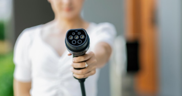 Focus hand pointing ev charger plug at camera with progressive blur background