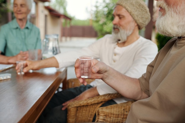 薬を入れた透明なカップを握っている年配の男性の手に焦点を当てます