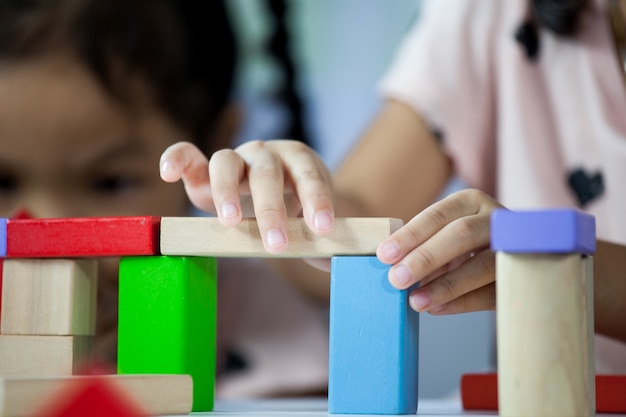 Metta a fuoco sulle mani della ragazza sveglia del piccolo bambino che gioca con i blocchi di legno variopinti nella stanza