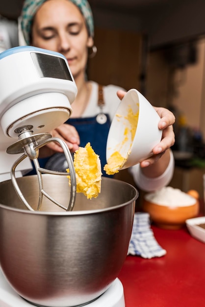 Focus on hands of female cook putting butter into bowl of electric mixer for the preparation of homemade argentinean alfajor