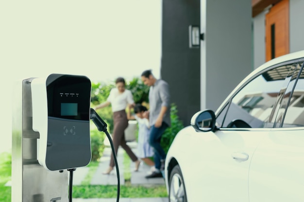 バック グラウンドで EV 車のぼかしプログレッシブ ファミリーのホーム充電ステーションに焦点を当てる