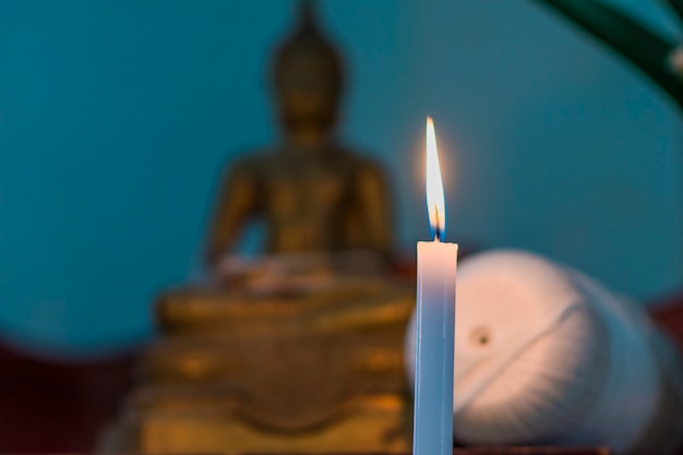 A focus image of a candle shining in the foreground and blurring the background of the Buddha image.