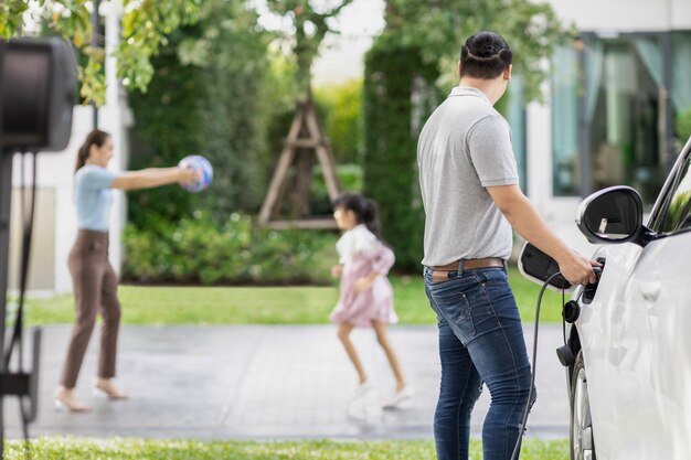 Focus image of progressive man charging EV car with his blur family background