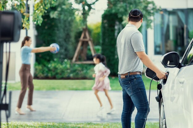 Focus image of progressive man charging EV car with his blur family background