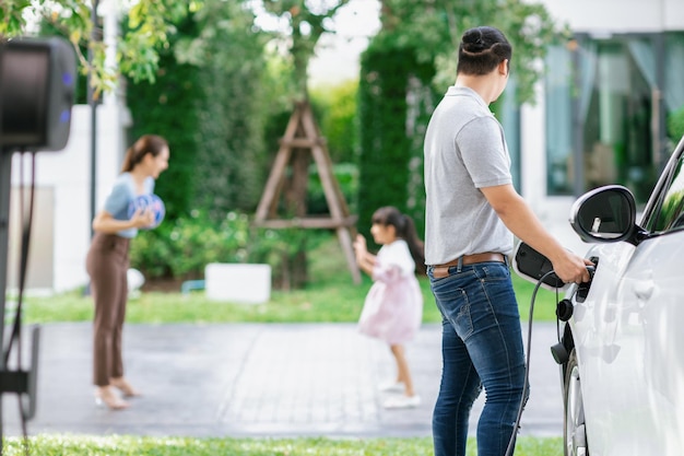 Focus image of progressive man charging EV car with his blur family background