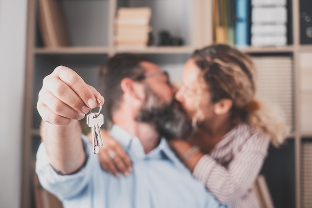 Focus on keys, held by excited young spouses homeowners. Happy married family couple celebrating moving in new house home , demonstrating keys, standing in apartment, real estate mortgage concept.