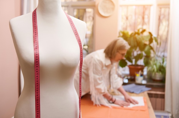 Photo focus on a mannequin and meter in fashion design studio on blurred background of a tailor working with fabric and sewing pattern creating new clothes