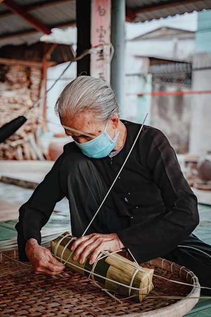 베트남 전통 드레스를 입은 노파에 초점을 맞춘 아오 바 바 포장 Tet 케이크 만들기 베트남 음력 설날 Tet 음식 야외 손으로 만들기