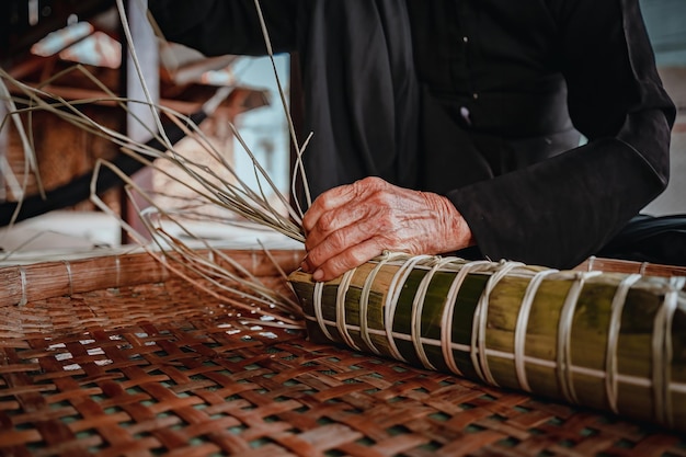 Focus old woman with traditional Vietnamese dress ao ba ba Making wrapping Tet Cake the Vietnamese lunar new year Tet food outdoor by hands