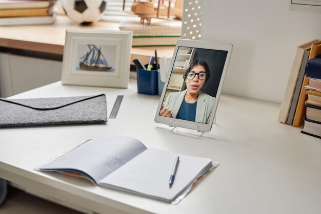 Focus op digitale tablet met docentenportret op tafel met open werkboek en schoolbenodigdheden