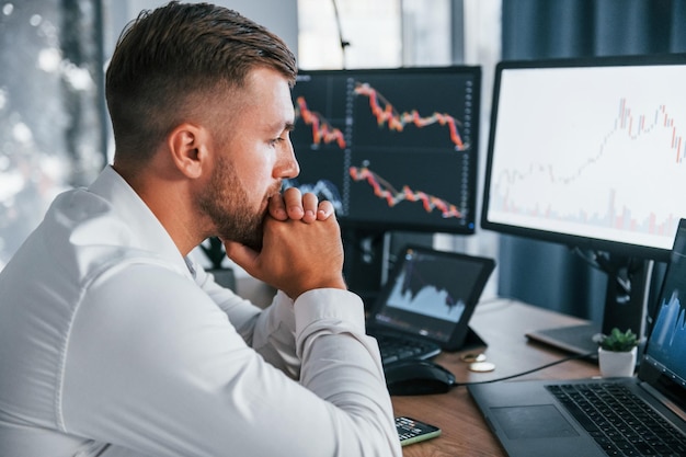 Focus op het werk Jonge zakenman in formele kleding zit op kantoor met meerdere schermen