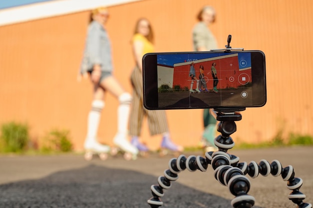 Focus op statief met smartphone tijdens video-opnamen van drie rolschaatsers