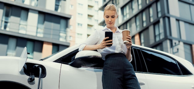 Focus progressive woman using phone and holding coffee at charging station