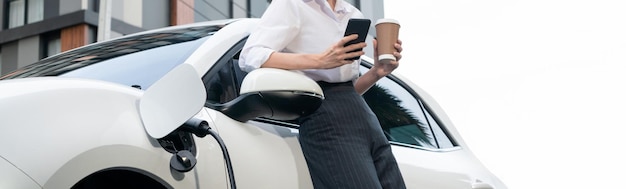 휴대폰을 사용하고 충전소에서 커피를 들고 있는 진보적인 여성에 초점을 맞춥니다.