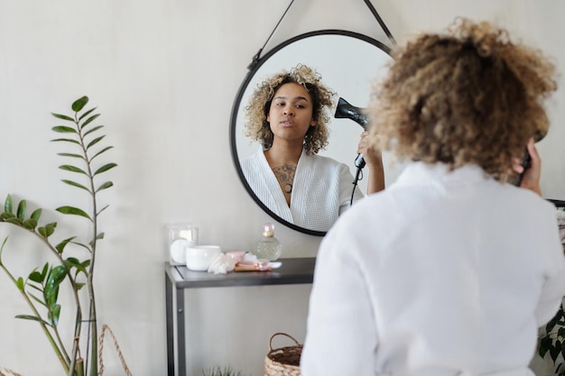 Focus on reflection in mirror of young black woman drying clean curly hair