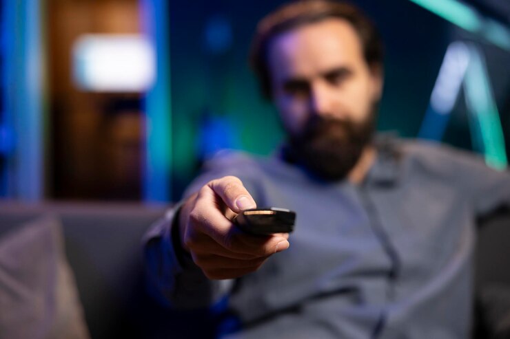 Photo focus on remote control held by viewer in blurry background at home on couch