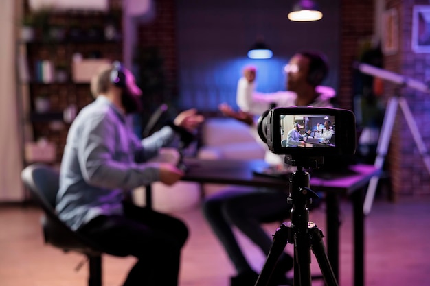 Photo focus shot on professional camera used to record podcast show with presenter and guest discussing in blurry background equipment in home studio used for live streaming broadcast