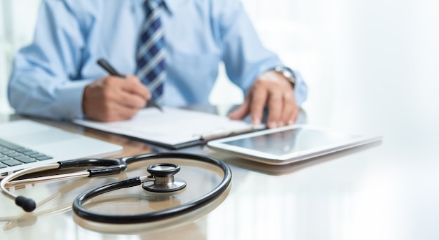 Photo focus on stethoscope. senior doctor male sitting working at the desk in medical clinic office