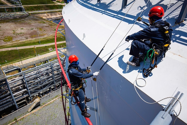 Focus top view male two worker down height tank roof rope\
access safety inspection of thickness storage tank gas\
propane.