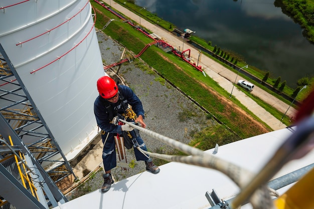 Foto messa a fuoco vista dall'alto lavoratore di sesso maschile verso il basso moschettone altezza fune tetto serbatoio nodo corrimano accesso fune ispezione di sicurezza dello spessore del tetto del serbatoio di stoccaggio.