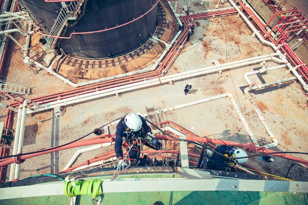 Foto messa a fuoco vista dall'alto lavoratore maschio giù altezza tetto del serbatoio accesso alla fune ispezione di sicurezza del petrolio greggio del serbatoio di stoccaggio dello spessore