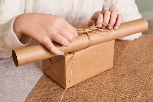 Focus on  woman's hands in white knitted sweater packaging box. Craft wrapping paper and natural twine. Happy holiday present, surprise. Gifts for boxing day