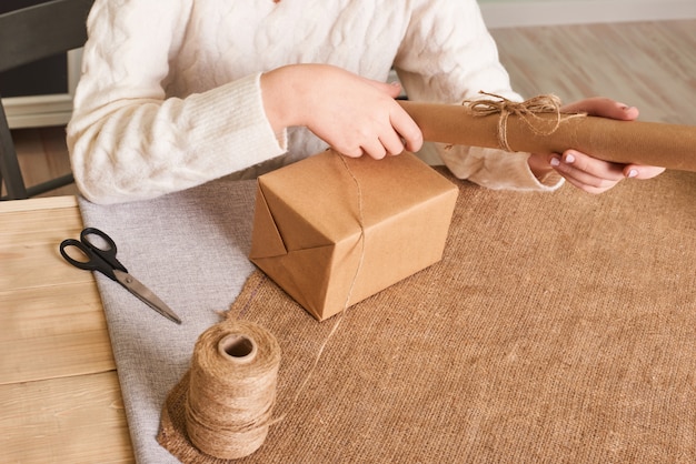 Focus on  woman's hands in white knitted sweater packaging box. Craft wrapping paper and natural twine. Happy holiday present, surprise. Gifts for boxing day