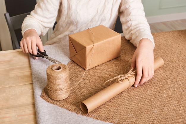 Foto focus sulle mani della donna in scatola da imballaggio maglione lavorato a maglia bianco. carta da regalo artigianale e spago naturale. buone vacanze, sorpresa. regali per il santo stefano