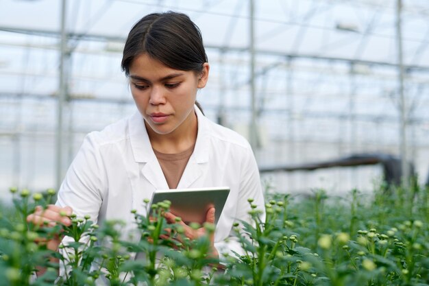 Focus on young female agronomist in labcoat standing in front of flowerbed