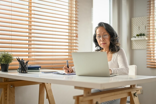 Una donna d'affari asiatica di 60 anni che lavora da casa utilizzando il laptop