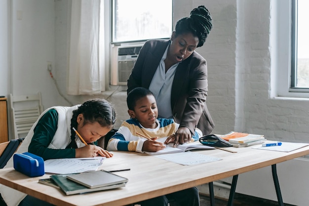 Focused African American female teacher in formal clothes standing near school desk with diverse pup