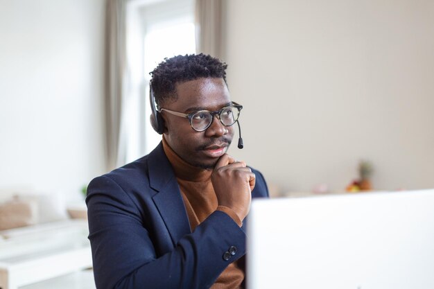 집중된 아프리카 남자는 노트북 화면을 보고 있는 마이크가 달린 헤드폰을 착용합니다.