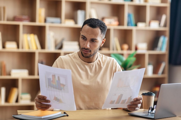 Focused arab man looking through documents checking reports while having online meeting on laptop