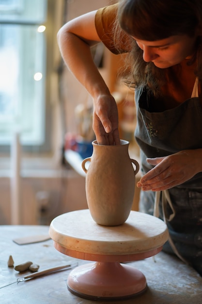 Focused artist woman moulding potter vase in studio owner of craft shop creating new pottery jug