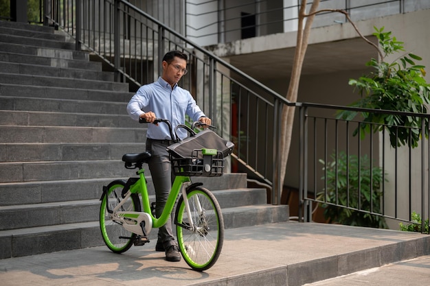 自転車で仕事に行くアジア人ビジネスマンが緑の自転車を押している