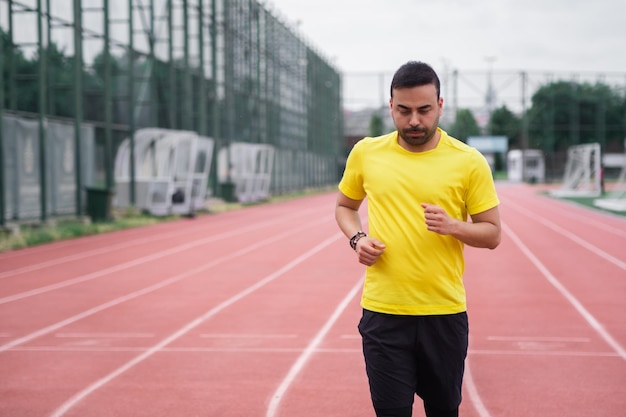 Focused athlete in color tshirt running along red track past soccer field preparing for important