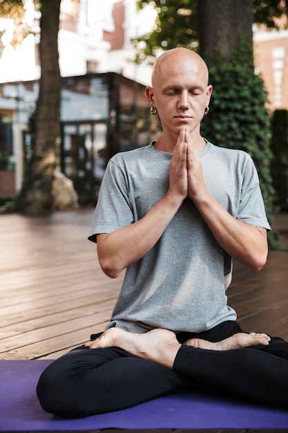 Focused attractive fitness yoga man meditating while sitting on a fitness mat outdoors