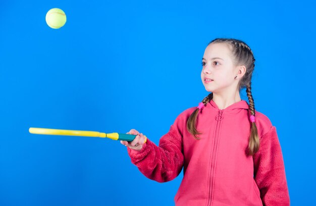 Focused on ball Girl adorable child play tennis Practicing tennis skills and having fun Athlete kid tennis racket on blue background Active leisure and hobby Tennis sport and entertainment