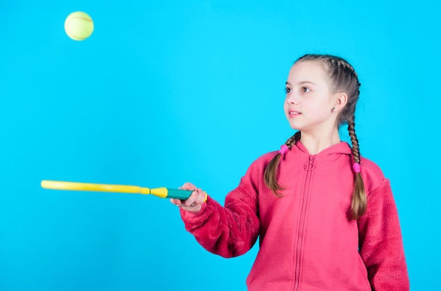 Focused on ball Girl adorable child play tennis Practicing tennis skills and having fun Athlete kid tennis racket on blue background Active leisure and hobby Tennis sport and entertainment