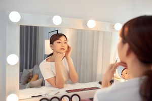 Focused beautiful young asian woman looking at herself in the mirror