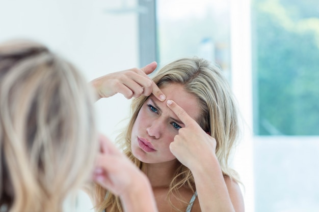 Focused beautiful young woman looking at herself in the bathroom mirror at home