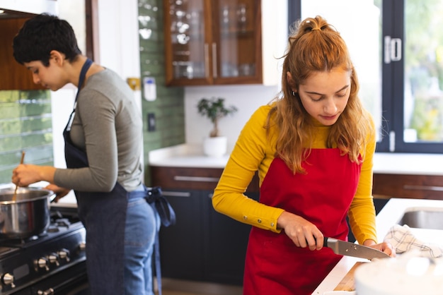 Foto coppia lesbica biraciale concentrata che cucina sul fornello e taglia le verdure in cucina