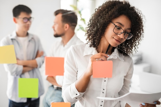 Focused black lady reading documents near multiracial coworkers during brainstorm