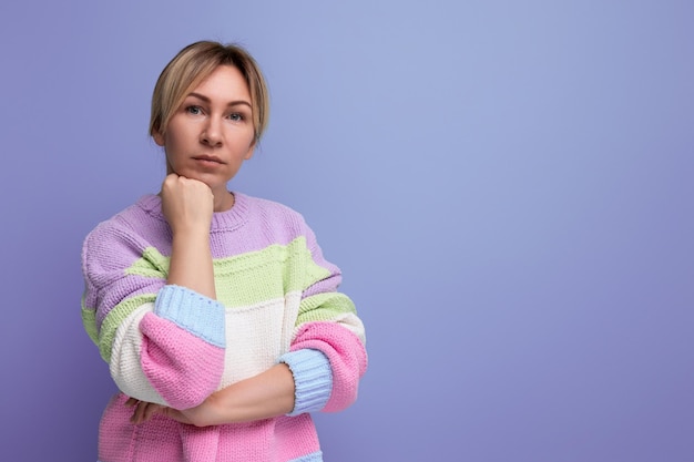 Focused blond young woman looking seriously at camera on purple background with copy space