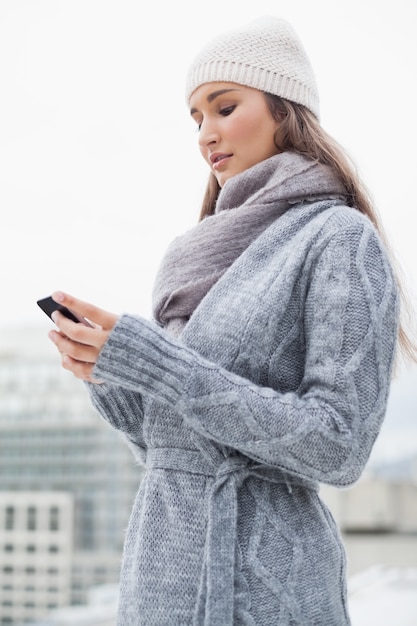 Brunette messo a fuoco con i vestiti di inverno su invio di messaggi di testo