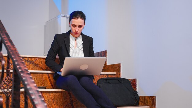 Focused business employee working on to finish a corporate job deadline at late hours sitting on staircase of business building. Serious tired entrepreneur doing overtime at financial project.