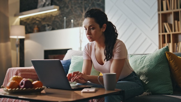 Focused business woman typing laptop sitting couch freelancer working remotely